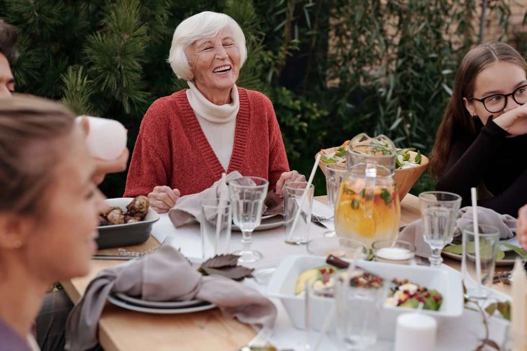 Vyresnio amžiaus moteris juokiasi prie pietų stalo